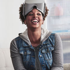 Smiling black girl in a jean jacket and stripped shirt wearing grey oculus go virtual reality headset on her forehead